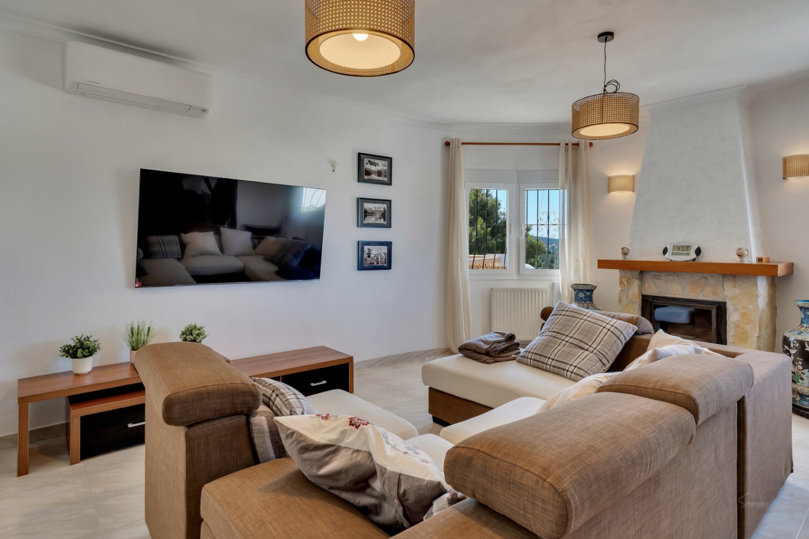Bright living area featuring a stone fireplace, split-system AC, and natural fiber pendant lighting. Includes a large modular sofa and wall-mounted television.