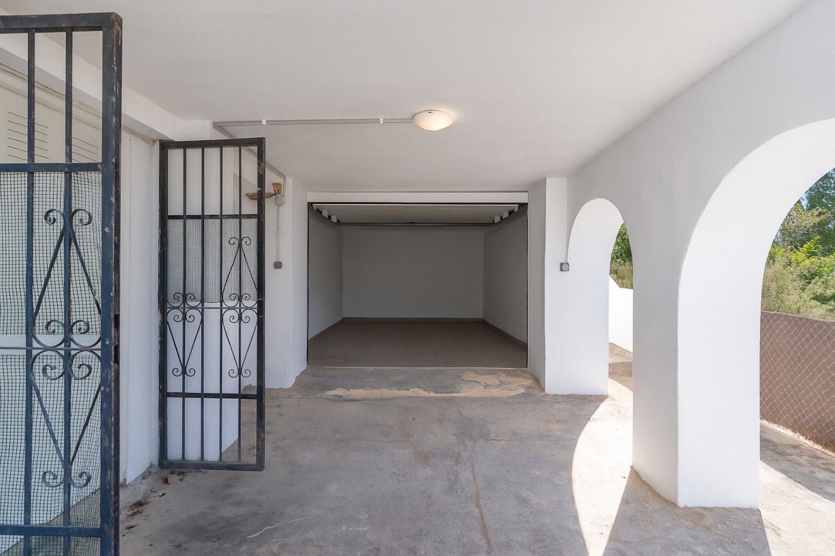 Covered parking area featuring white Mediterranean arches, a wrought-iron gate, and an integrated garage with tiled flooring.