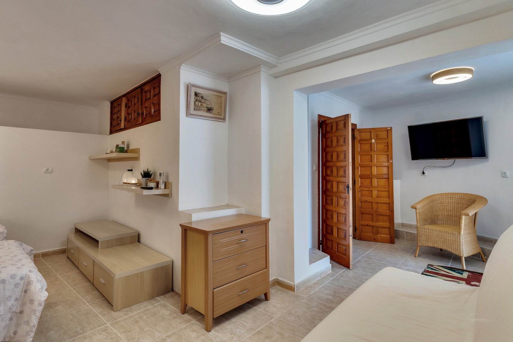 Lower-level bedroom featuring ceramic tile flooring, traditional wooden doors, a seating area with a wicker chair, and integrated storage solutions.