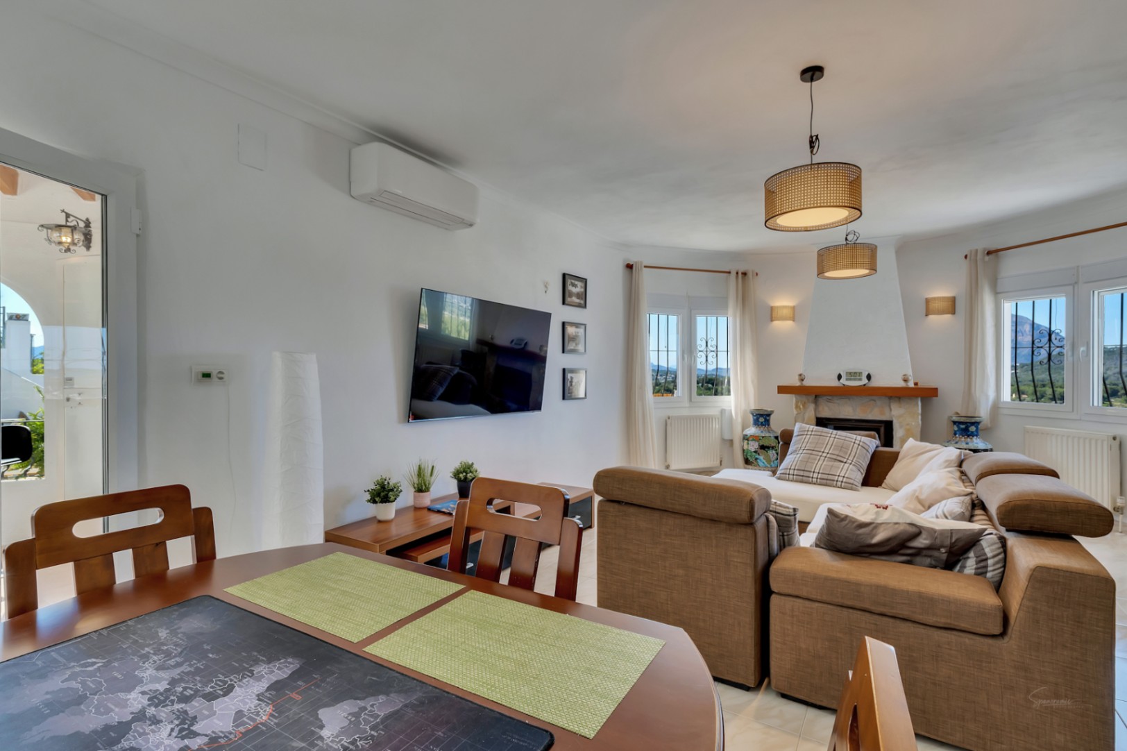 Luminous living area featuring a stone fireplace, large sectional sofa, and split air conditioning. Windows provide natural light and views of the Montgó mountain.