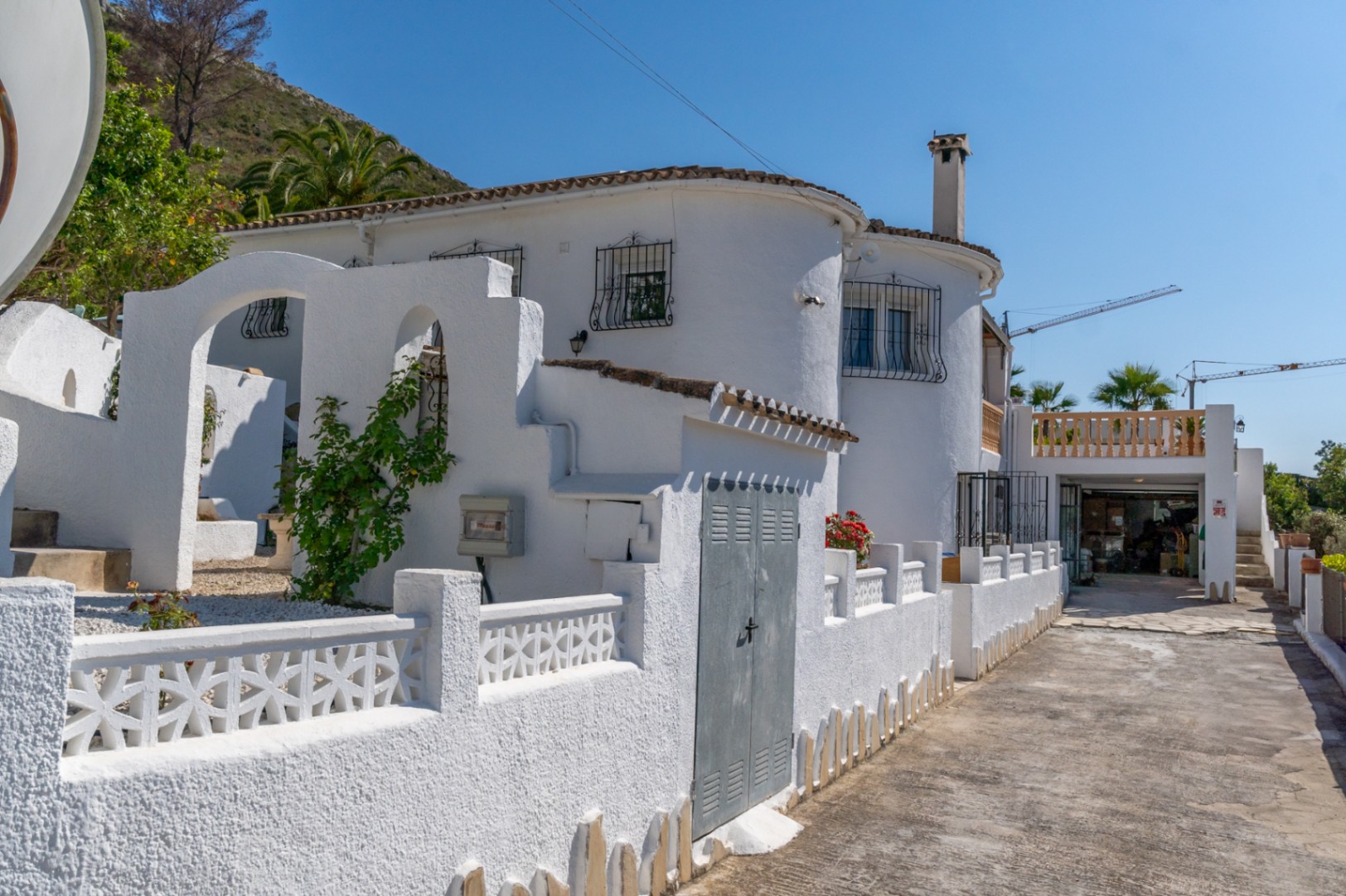 Mediterranean-style exterior featuring textured white walls, arched architectural details, wrought iron window guards, and a paved driveway leading to the garage.