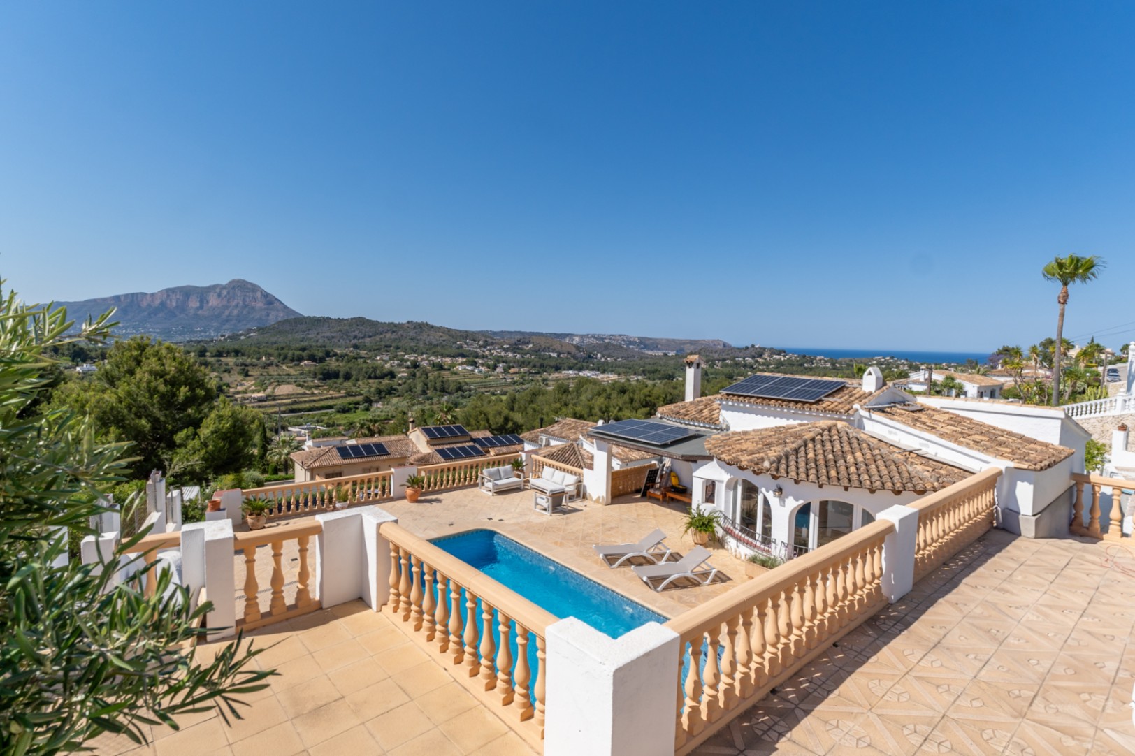 Panoramic view from the upper terrace featuring the swimming pool, solar panel installation, and expansive views of the Montgó mountain and Mediterranean Sea.