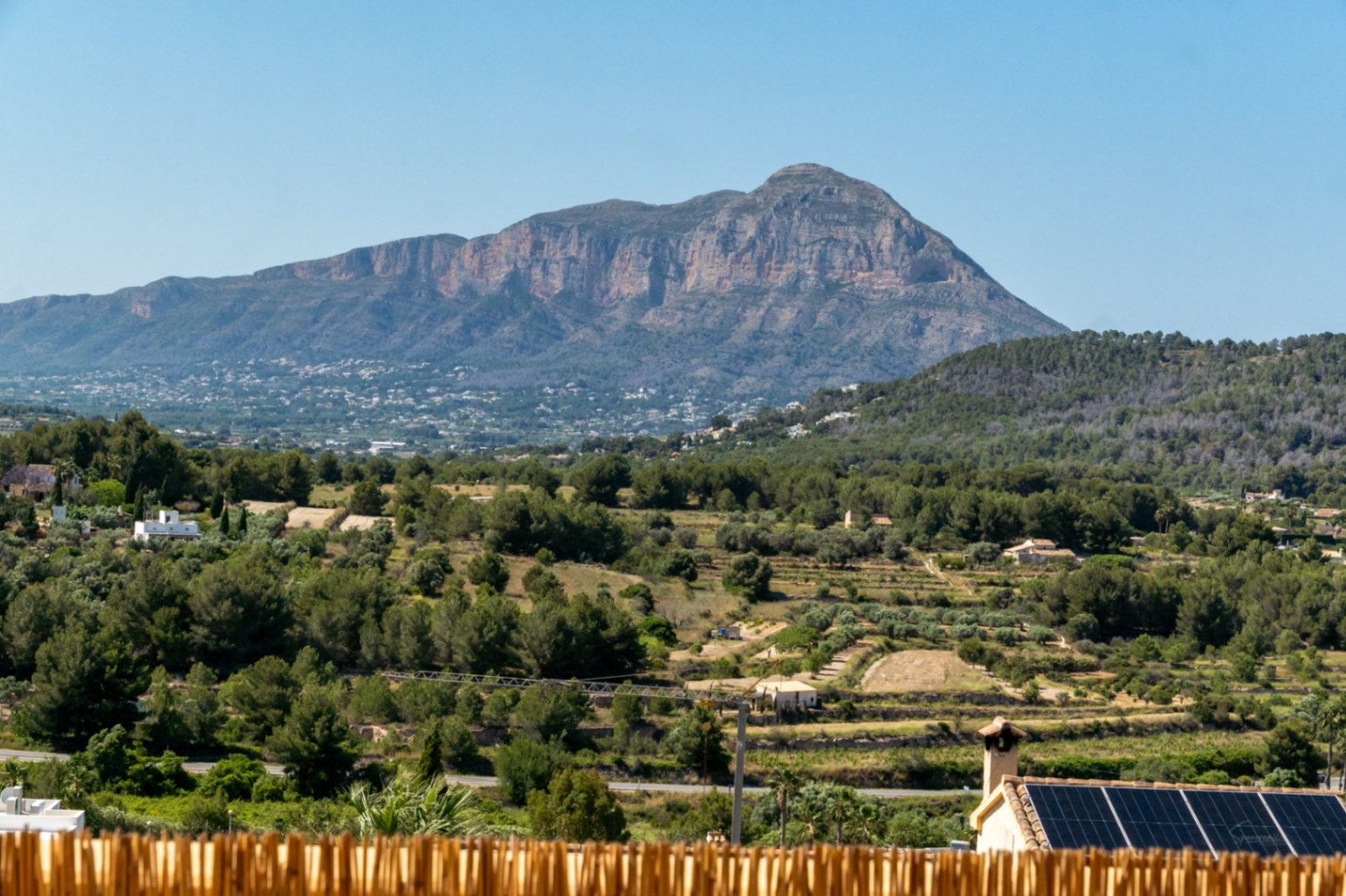 Panoramic views of the Montgó mountain massif overlooking a lush valley with Mediterranean vegetation and residential rooftops equipped with solar panels.
