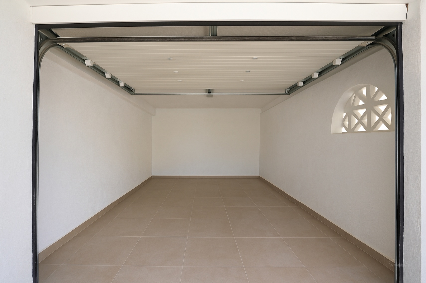 Private garage featuring tiled flooring, white walls, and an automatic sectional door. A decorative arched window provides natural light to the space.