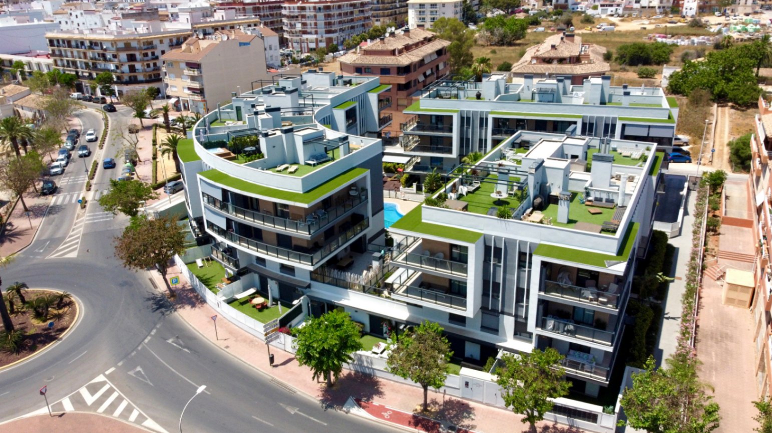 Aerial view of the modern residential complex featuring curved architecture, landscaped rooftop terraces, and a central swimming pool in a prime urban location.