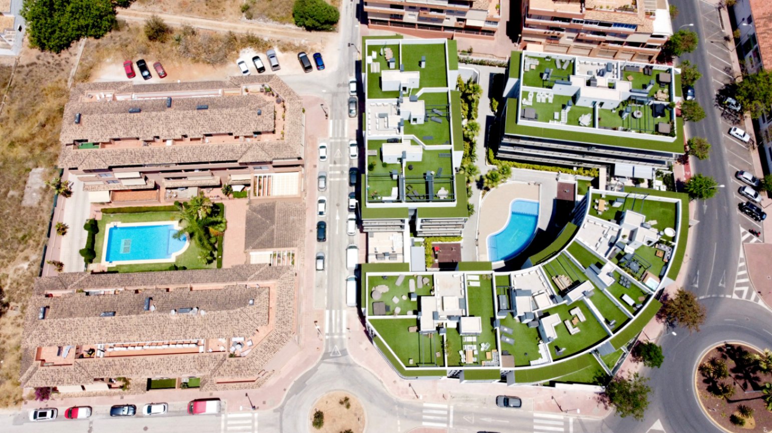 Aerial view of the modern residential complex featuring landscaped rooftops, contemporary architecture, and a central curved swimming pool area.