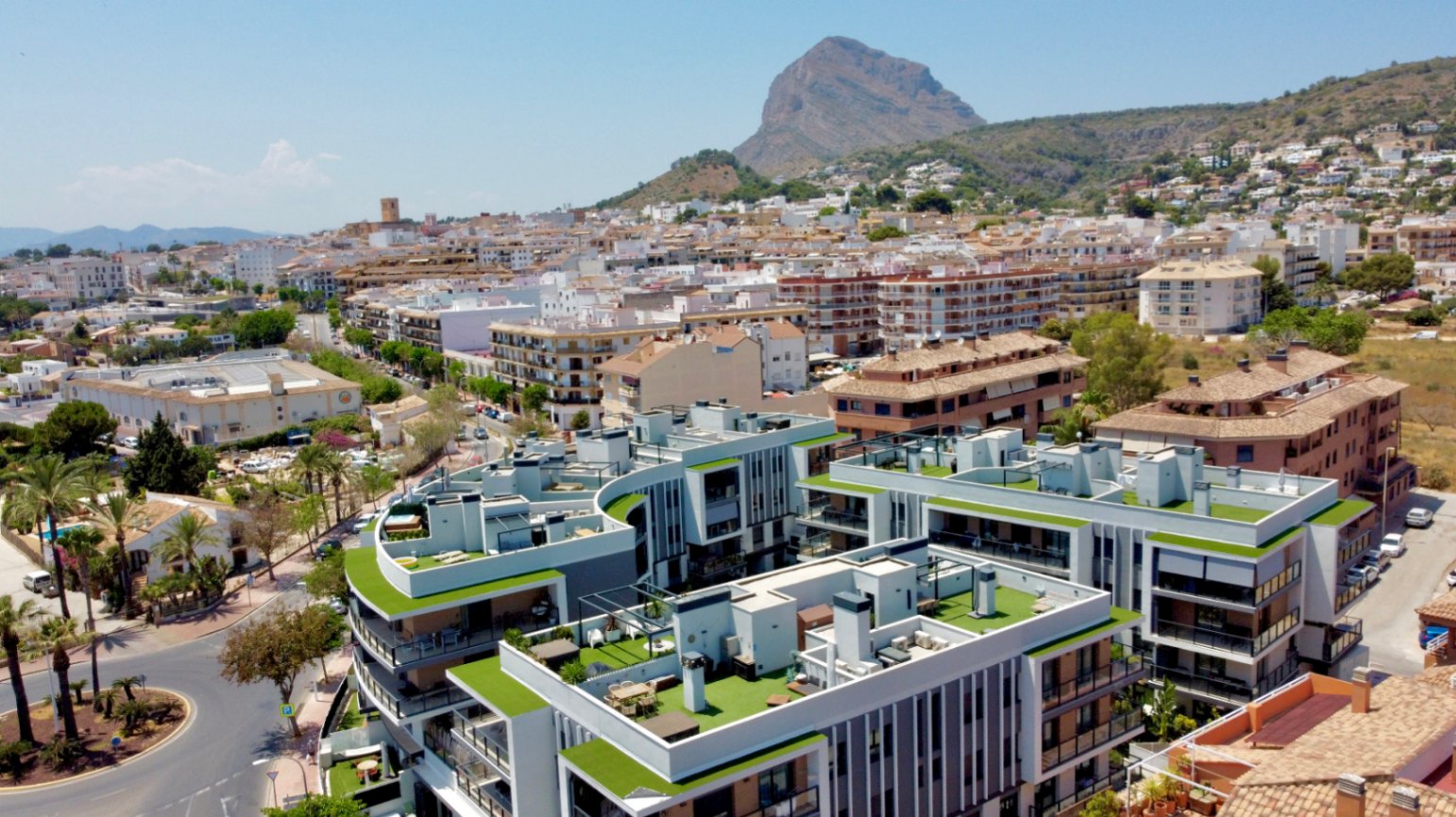 Aerial view of the modern residential complex in Jávea, featuring rooftop terraces with artificial turf and the iconic Montgó mountain in the background.