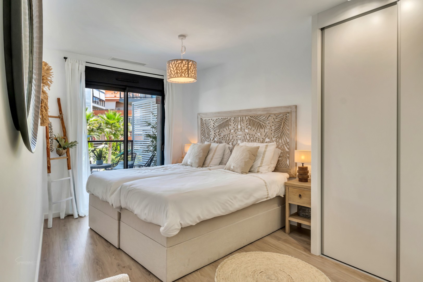 Bright bedroom featuring a carved wooden headboard, built-in wardrobes, and direct access to a private terrace overlooking Mediterranean greenery.