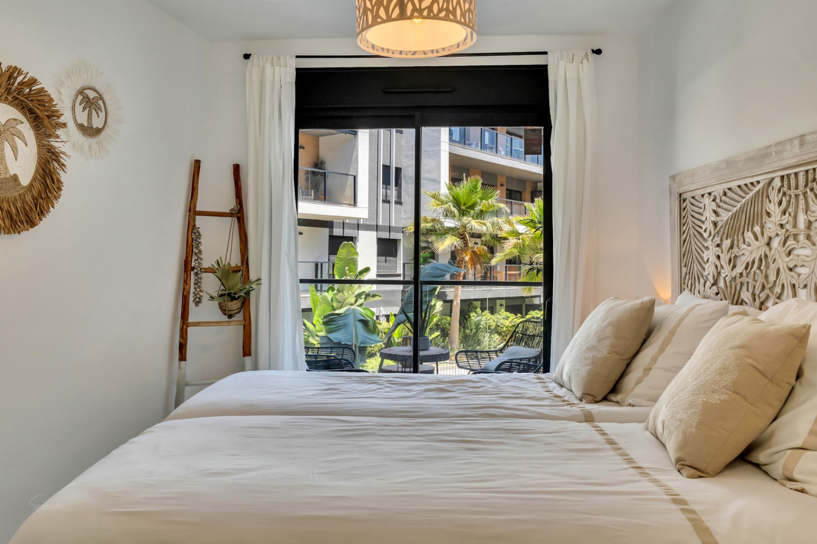 Bright bedroom featuring an ornate carved wooden headboard, Mediterranean decor, and large glass doors opening onto a private terrace with garden views.