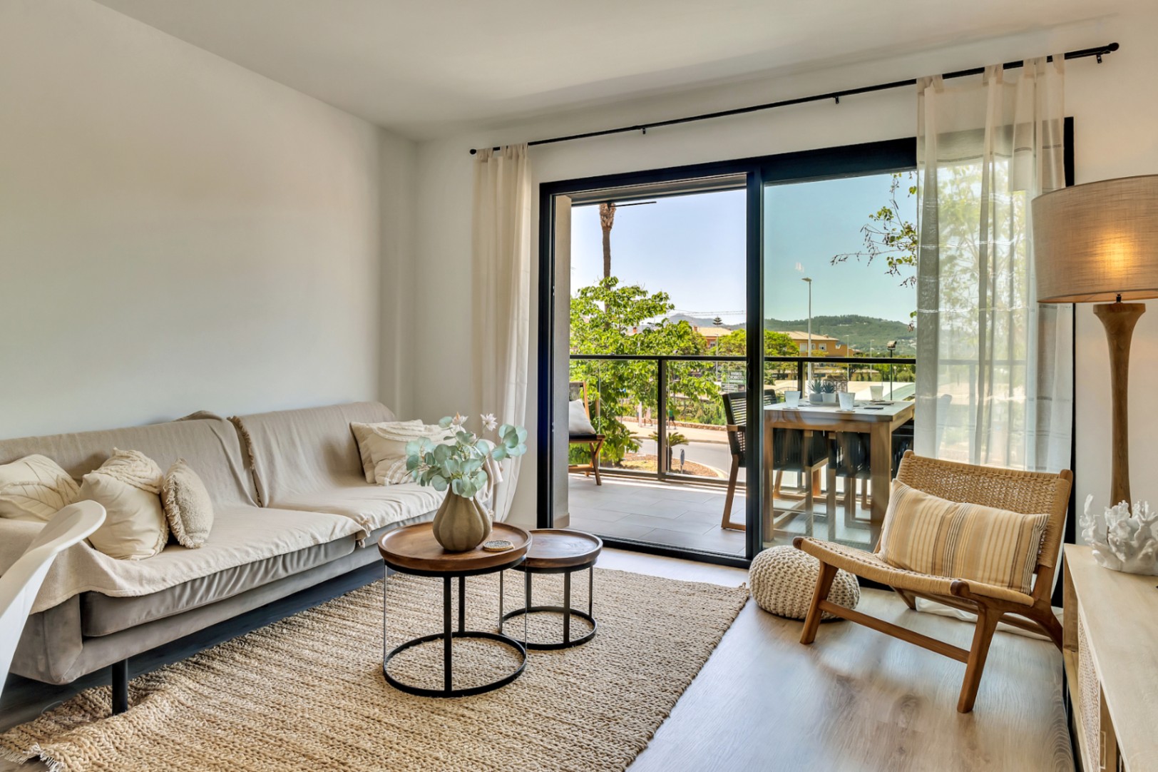 Bright living area featuring neutral-toned furniture, wooden flooring, and large sliding doors opening onto a private terrace with an outdoor dining set.