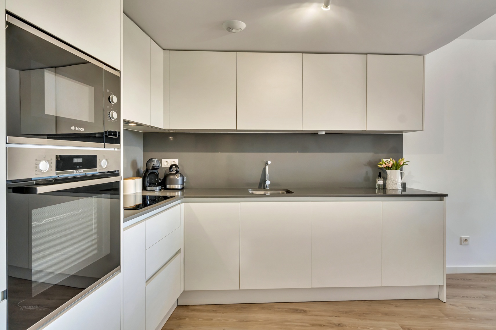 Modern minimalist kitchen featuring handle-less white cabinetry, anthracite grey countertops, and integrated Bosch appliances including a built-in oven and microwave.