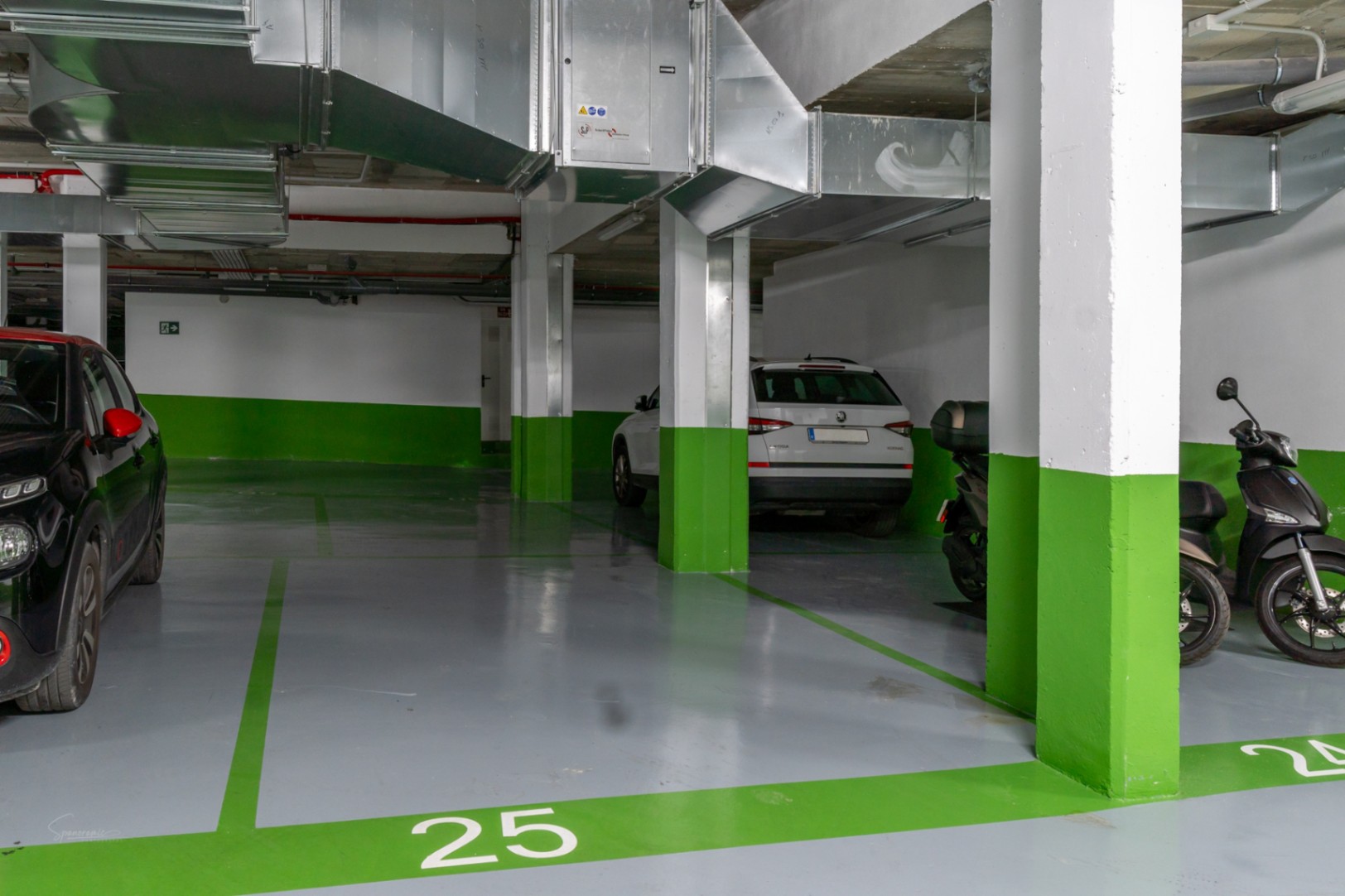 Numbered underground parking space featuring grey epoxy flooring, green accents, and exposed modern ventilation systems for a clean, functional design.
