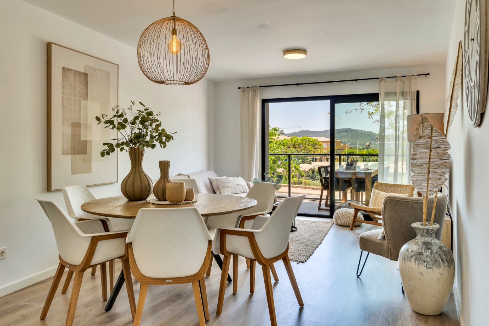 Open-concept living and dining area featuring a round wooden table, designer pendant lighting, and large sliding doors opening to a terrace with scenic views.