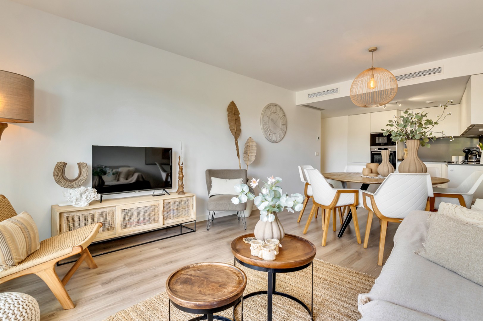 Open-concept living space featuring light wood flooring, natural fiber accents, and a modern kitchen with integrated appliances and minimalist white cabinetry.