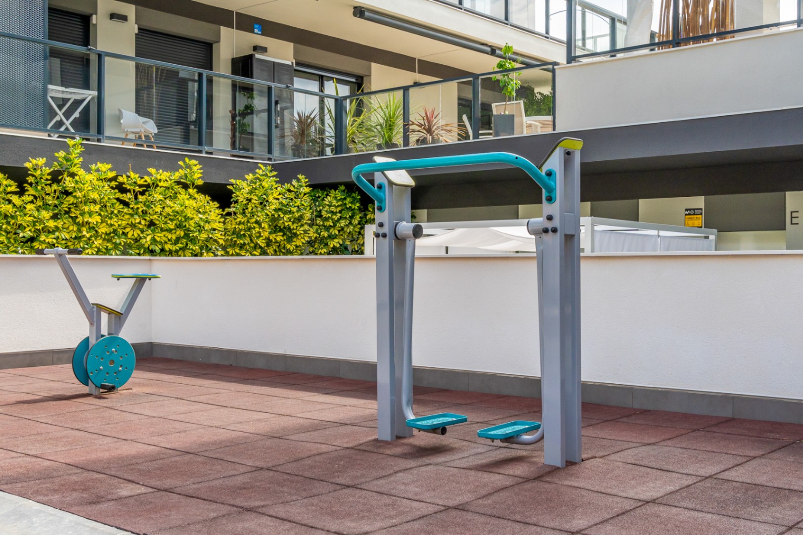 Outdoor fitness area featuring cardio equipment on safety rubber flooring, set within the common areas of the modern residential complex.