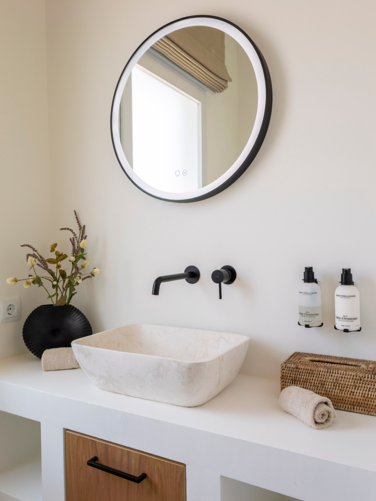 Bathroom detail featuring a stone sink, matte black fixtures, and a round mirror with integrated lighting.