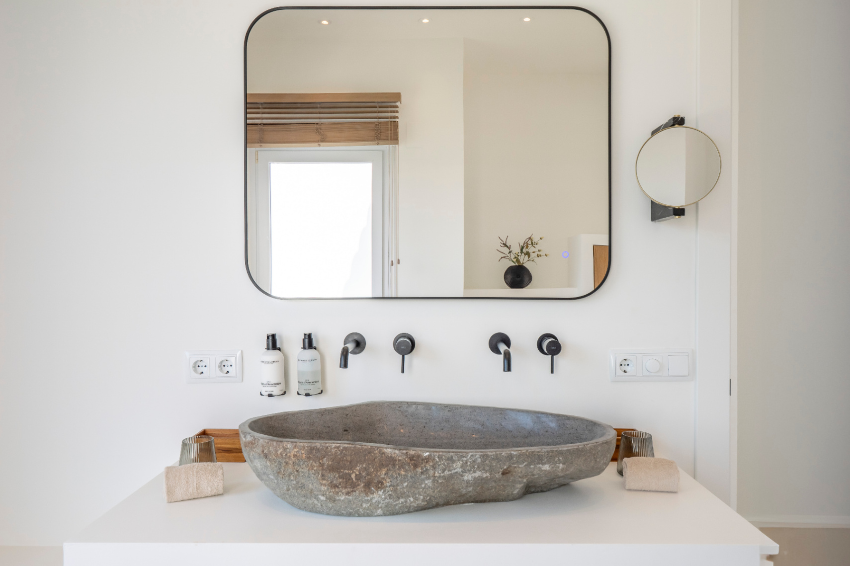 Bathroom detail with natural stone sink and matte black faucets. Rectangular mirror with integrated lighting.