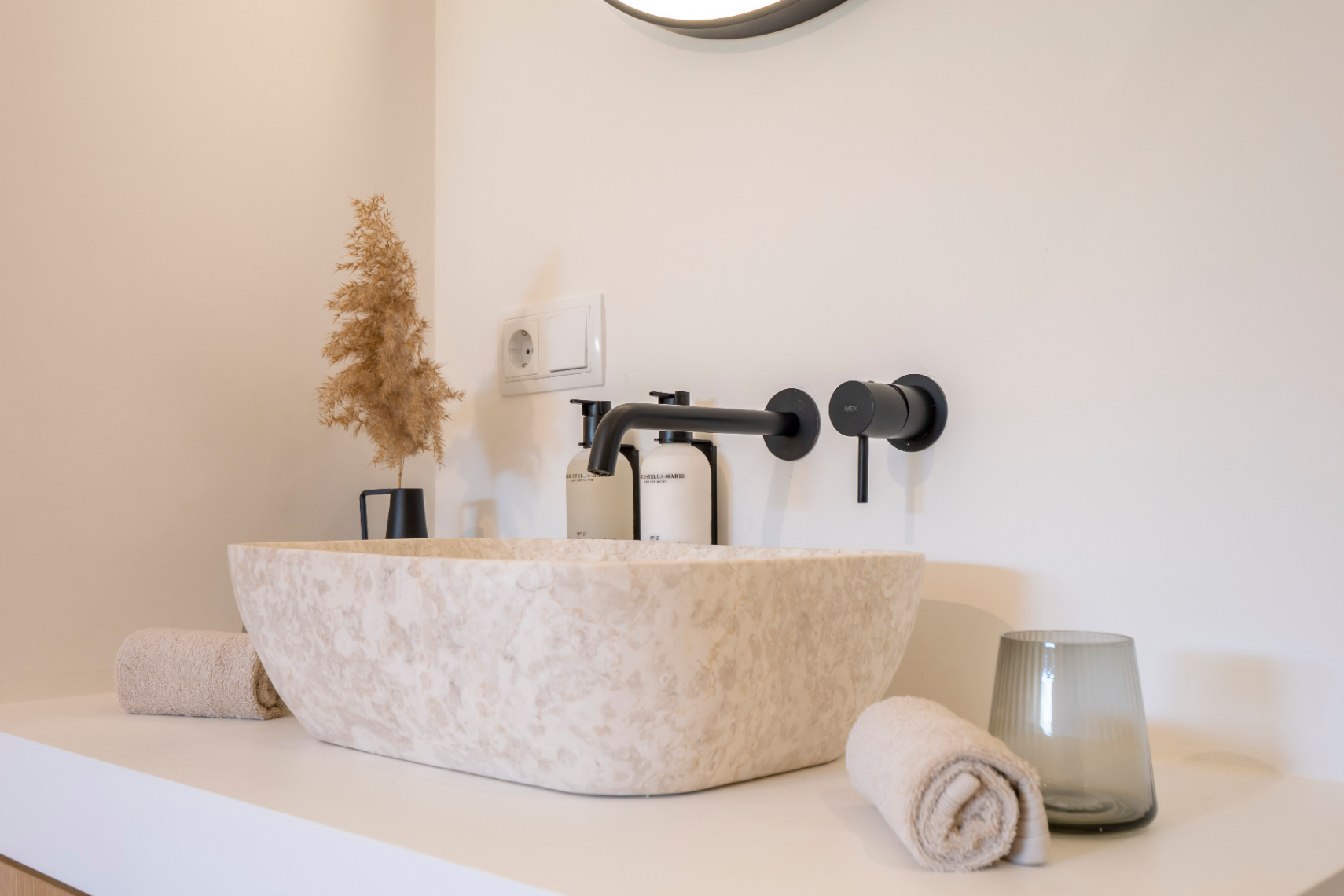Bathroom detail with natural stone sink and matte black fixtures. Minimalist decor with matching towels.