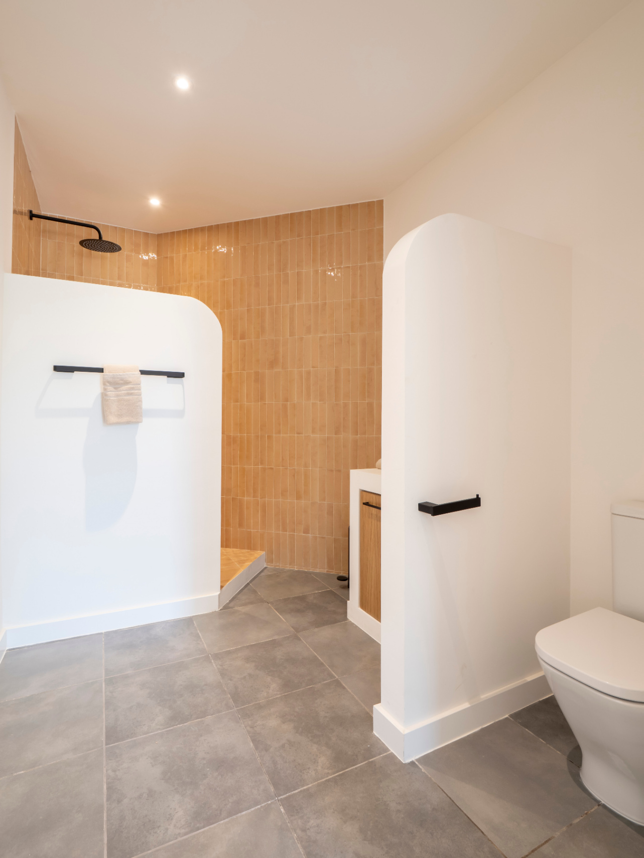 Bathroom with walk-in shower and ochre-colored tiles. Wood vanity and gray tiled floor.