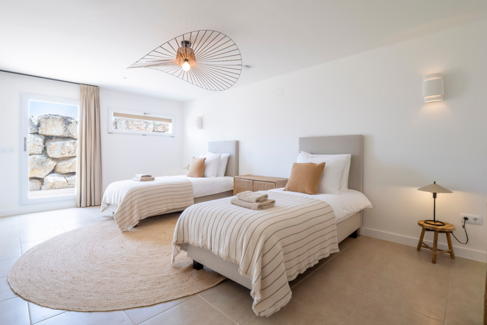 Bright bedroom with twin beds, jute rug, and designer light fixture.