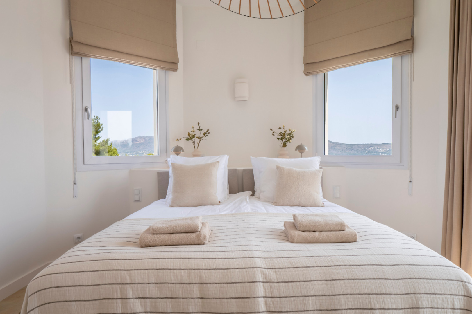 Bright bedroom with two windows offering exterior views. Double bed with striped bedding and folded towels.