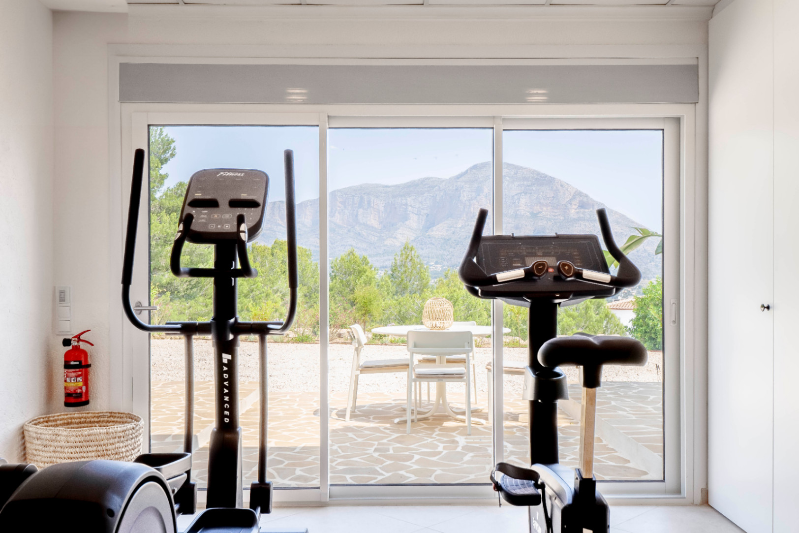 Bright gym with mountain views, equipped with stationary bike and elliptical trainer.
