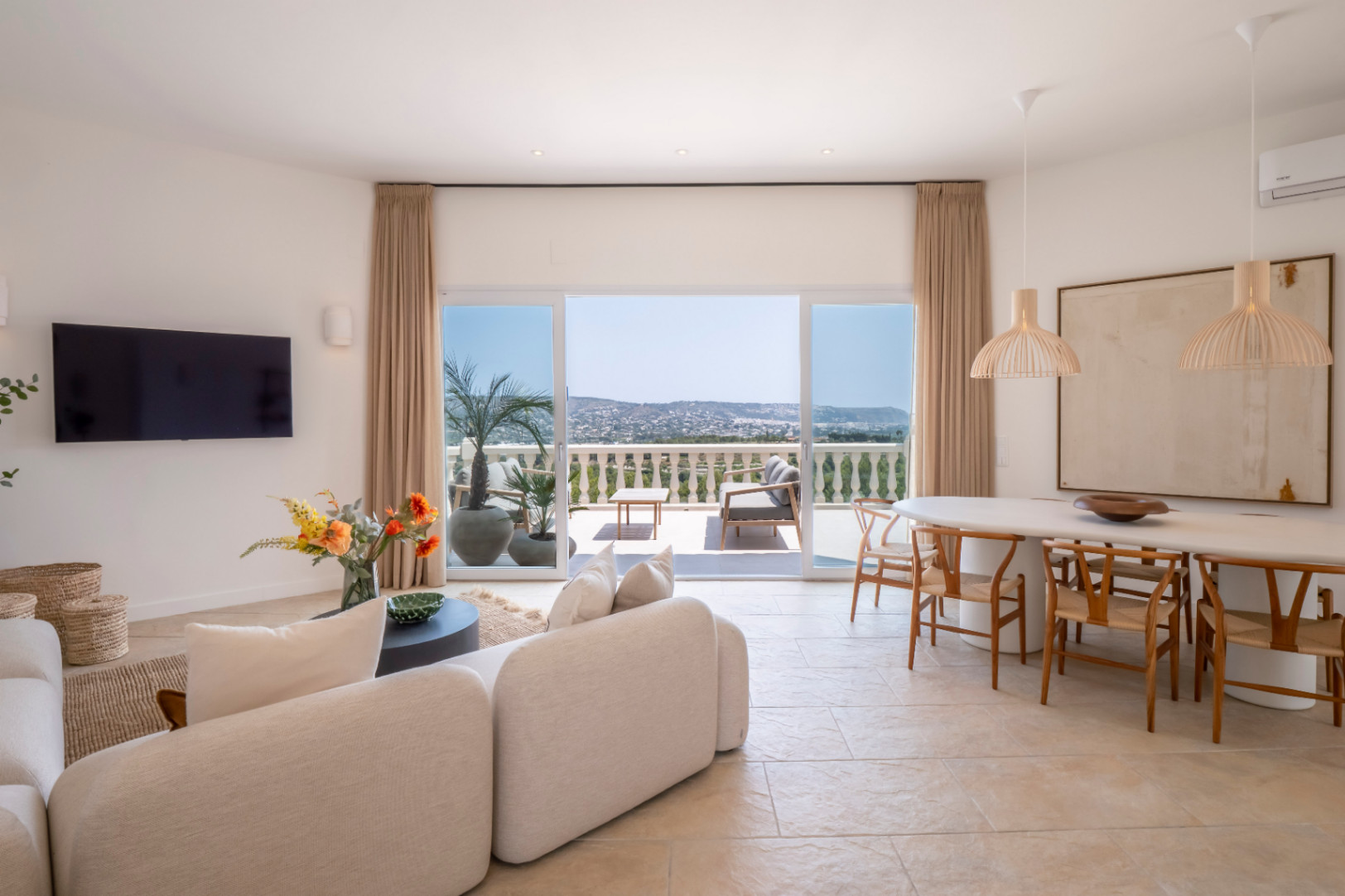 Bright living-dining area with terrace access and panoramic views. Modern design with light furniture and natural accents.