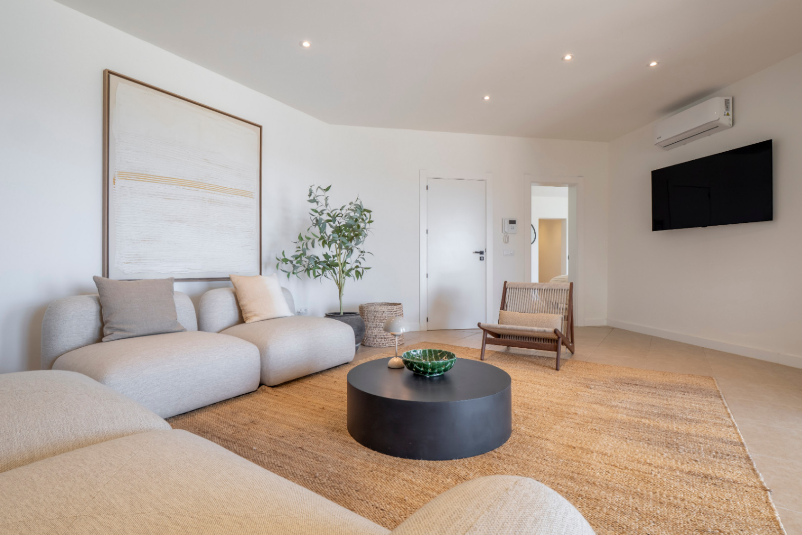 Bright living room with modular sofa, jute rug, and black circular coffee table. Minimalist decor and natural light.
