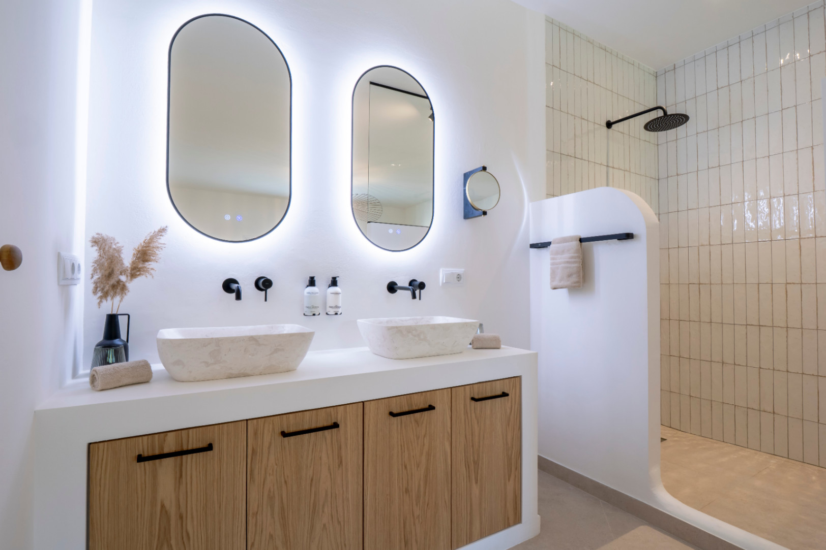 Elegant bathroom with stone sinks, oval mirrors with lights, and a shower with vertical tiles.