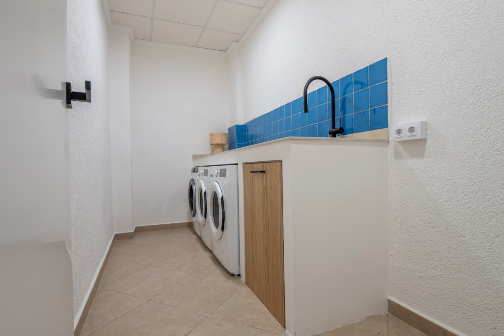 Functional laundry room featuring blue tiles, washing machines, and a light wood countertop.
