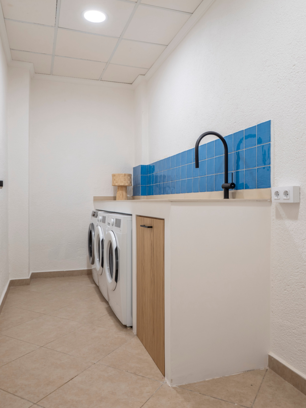 Functional laundry room with blue tile backsplash, beige countertop, white washing machines, and tiled floor.