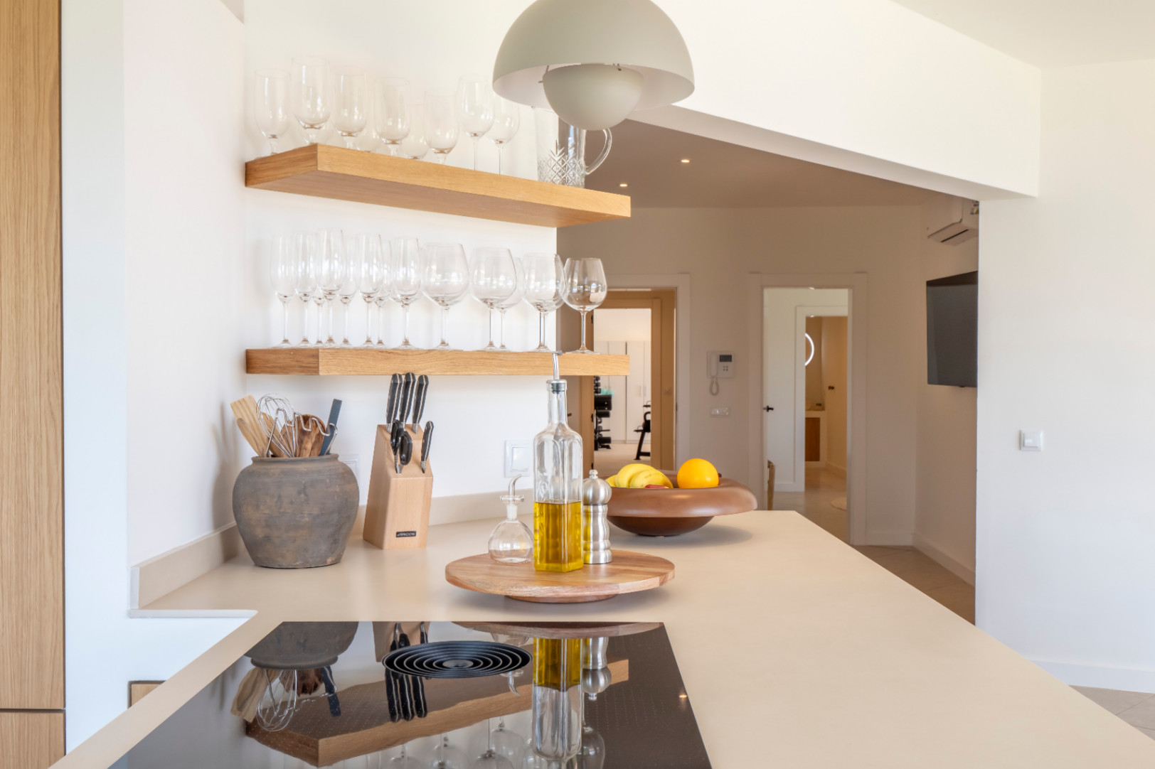 Kitchen detail: light wood shelves with glassware, beige countertop with induction hob, and minimalist decor.