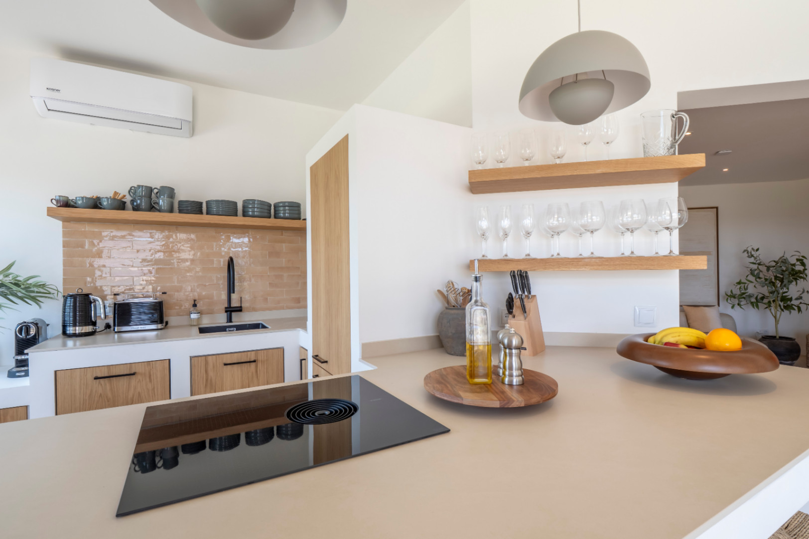 Kitchen detail with beige countertop, black ceramic hob, and light wood shelves displaying glassware.