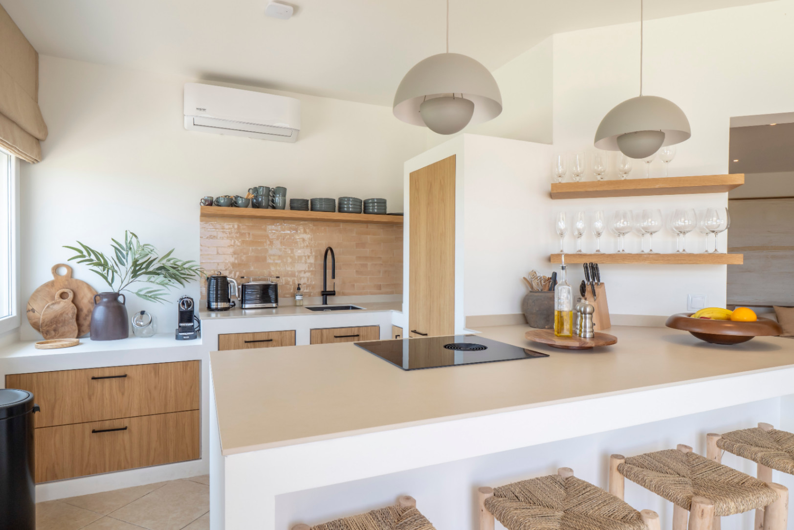 Kitchen detail with central island, wooden stools, and light countertop. Shelves display glassware and tableware.