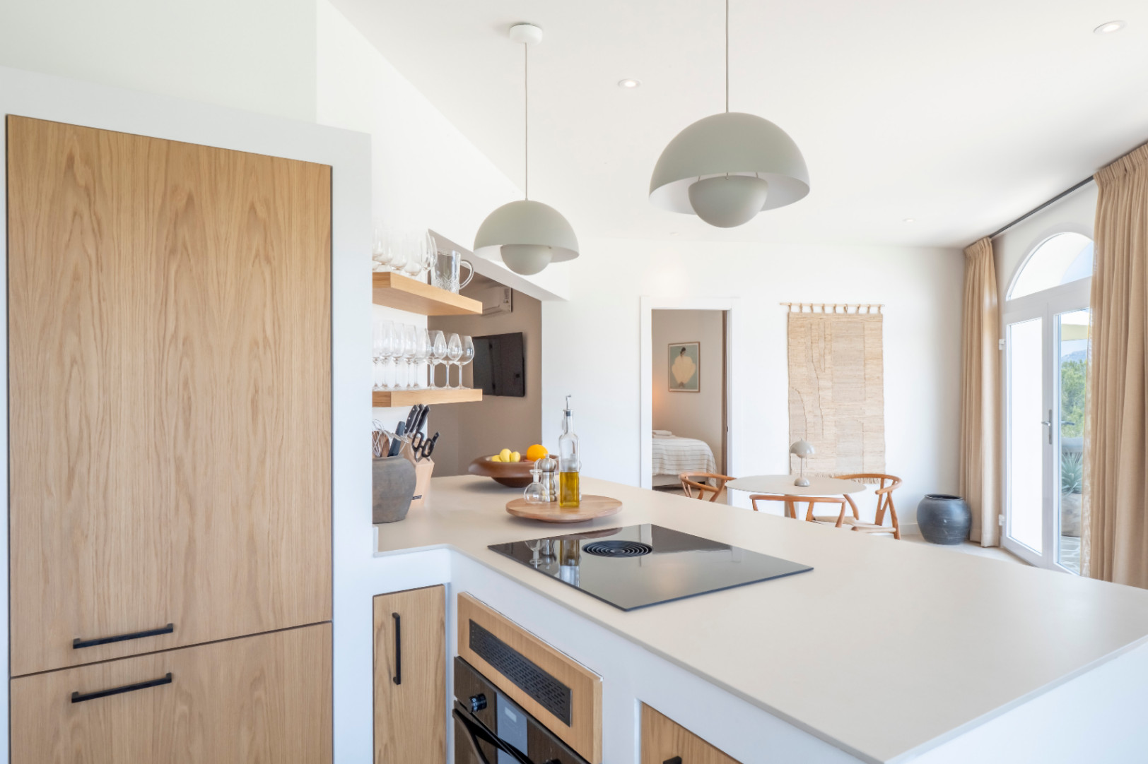 Kitchen detail with island, light wood paneled appliances, and open shelves displaying glassware.
