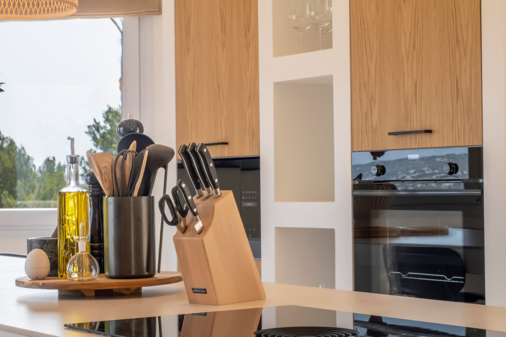 Kitchen detail with reflective countertop, wooden utensils, and light oak cabinets.