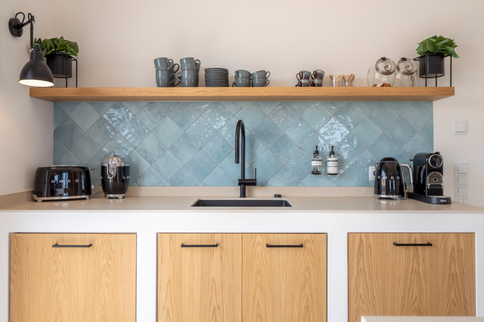 Kitchen detail with sink, turquoise tiles, and Smeg appliances. Light wood shelves.