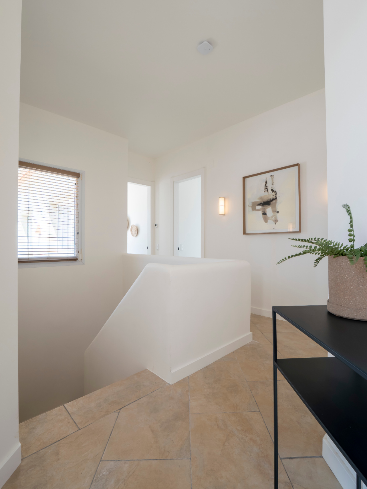 Landing detail with sand-toned tile floors, whitewashed railing, and abstract art adorning the wall.
