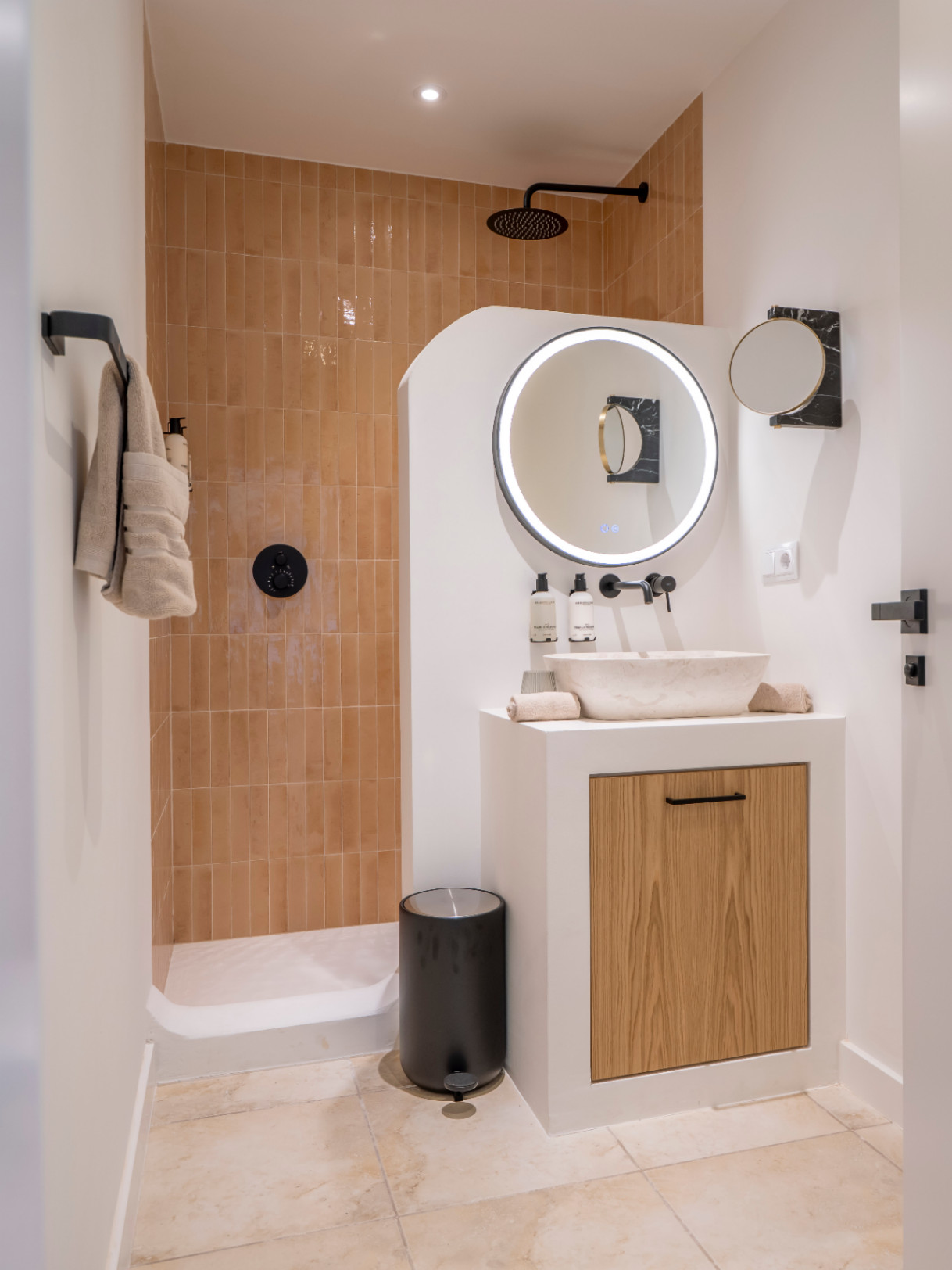 Modern bathroom detail with walk-in shower and stone sink on light wood cabinet.