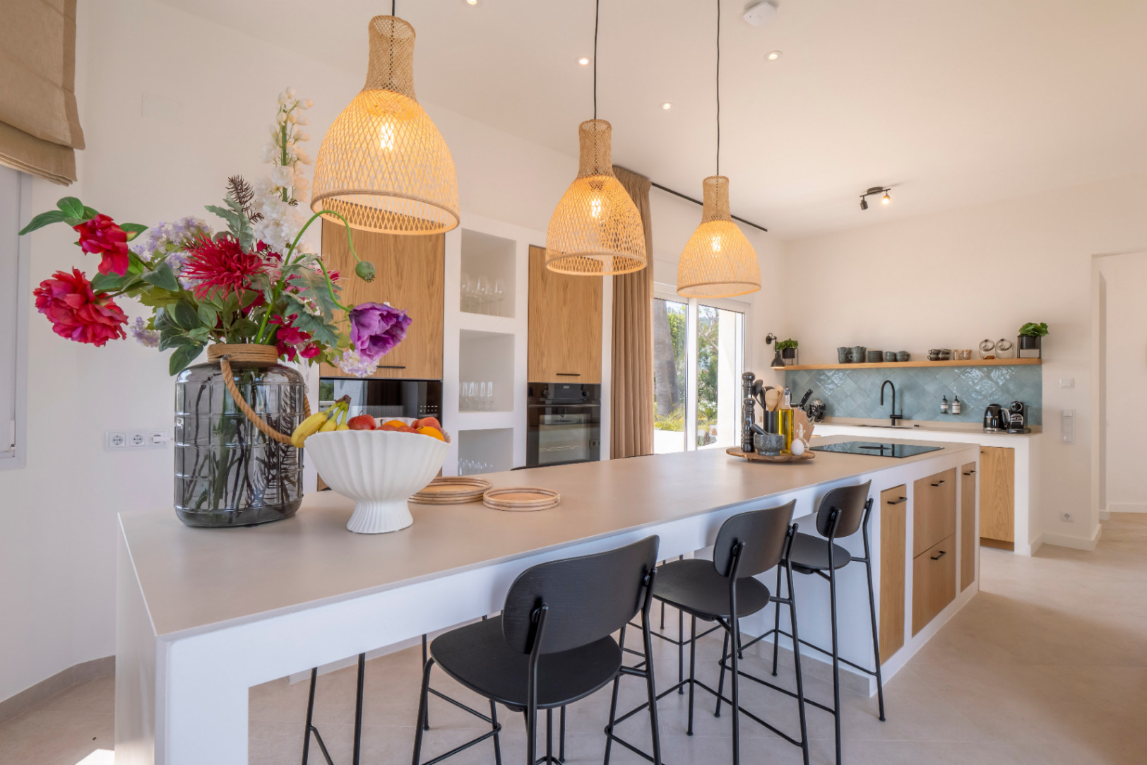 Modern kitchen with a central island, black stools, and wicker pendant lights.