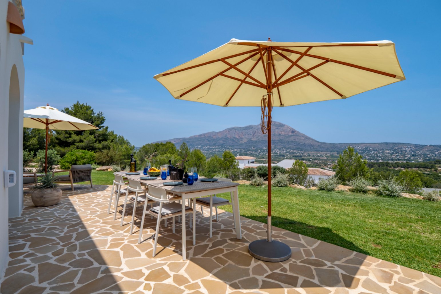 Outdoor dining area with irregular stone flooring and mountain views, under a parasol.