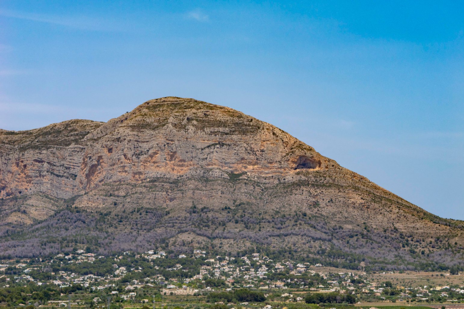 Panoramic view of Montgó mountain, featuring a visible cave and scattered houses at its base.