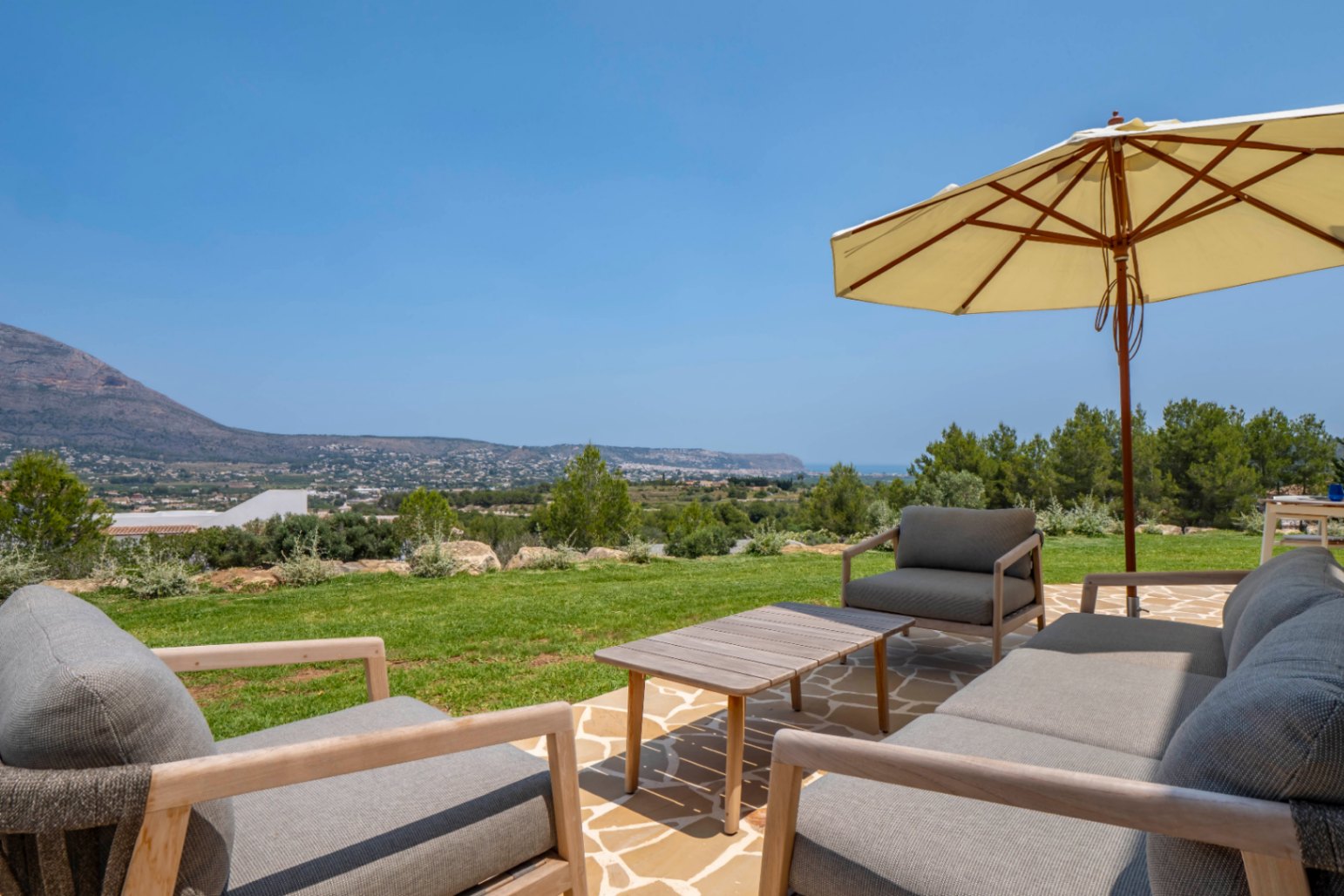 View terrace: stone and wood outdoor furniture under an umbrella, with Jávea landscape.
