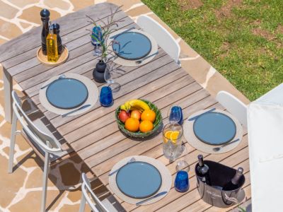 Outdoor dining table set with blue plates, glassware, and a fruit bowl, ready for garden enjoyment.