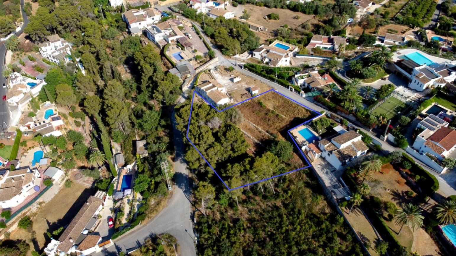 Aerial view of the 1,908 m² urban plot outlined in blue, featuring a mix of cleared land and mature pine trees within an established residential neighborhood.