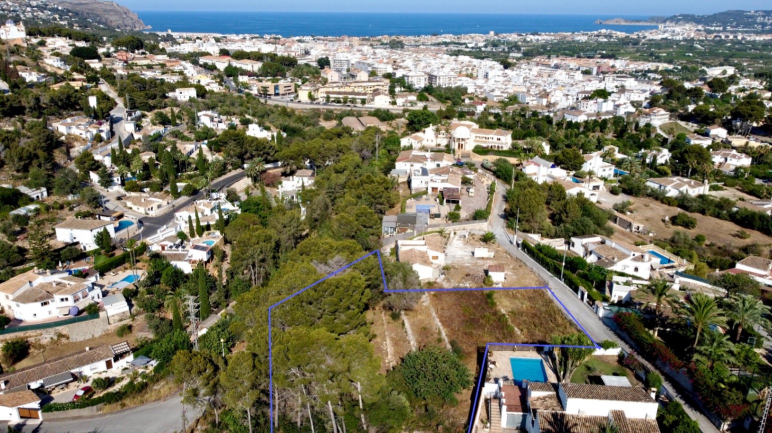 Aerial view of the blue-outlined plot, featuring native pine trees and a strategic location offering panoramic views of the Mediterranean Sea and Jávea town.