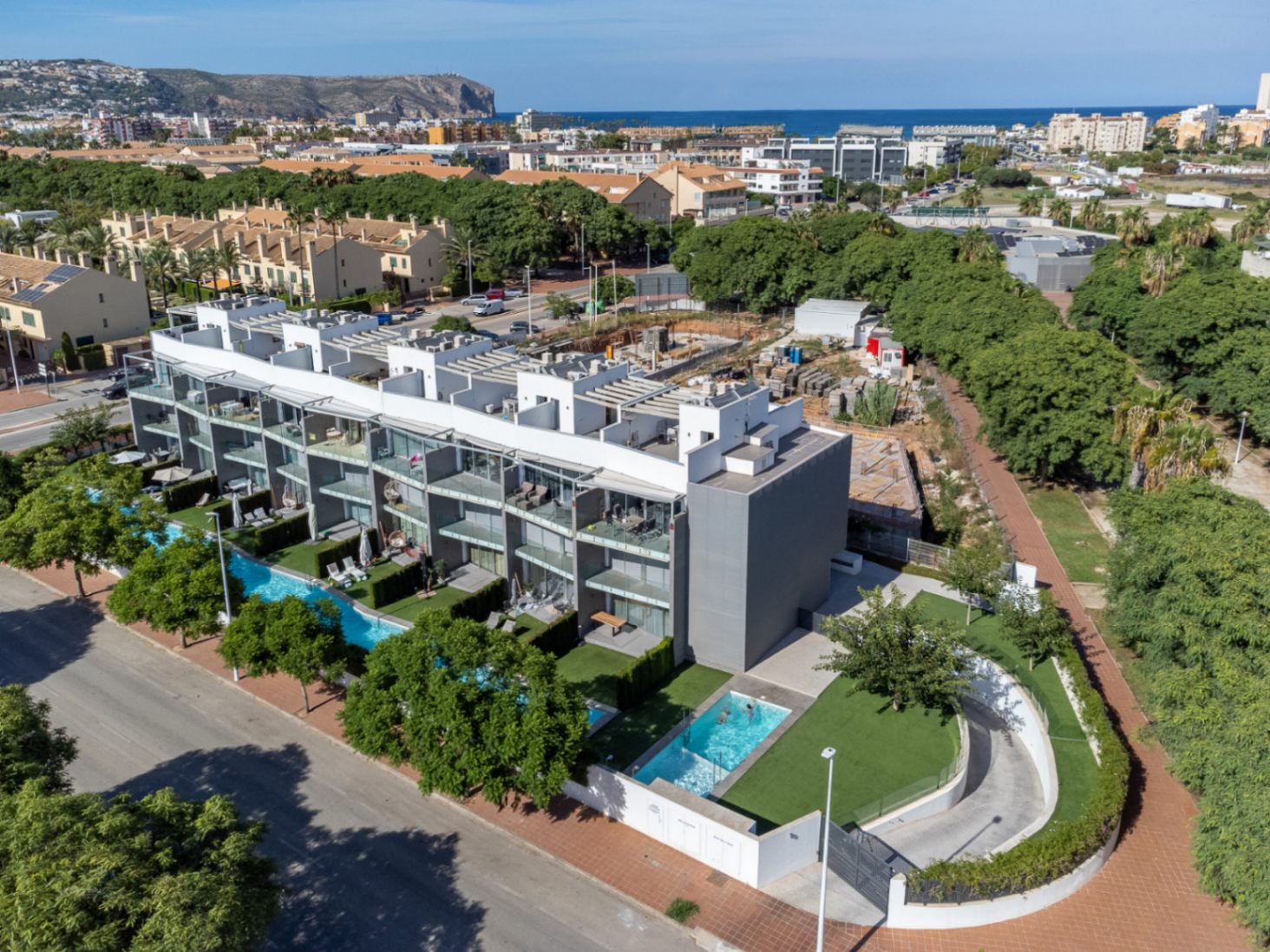 Aerial view of the modern residential complex featuring communal swimming pools, private gardens, and underground parking access near the Mediterranean coast.