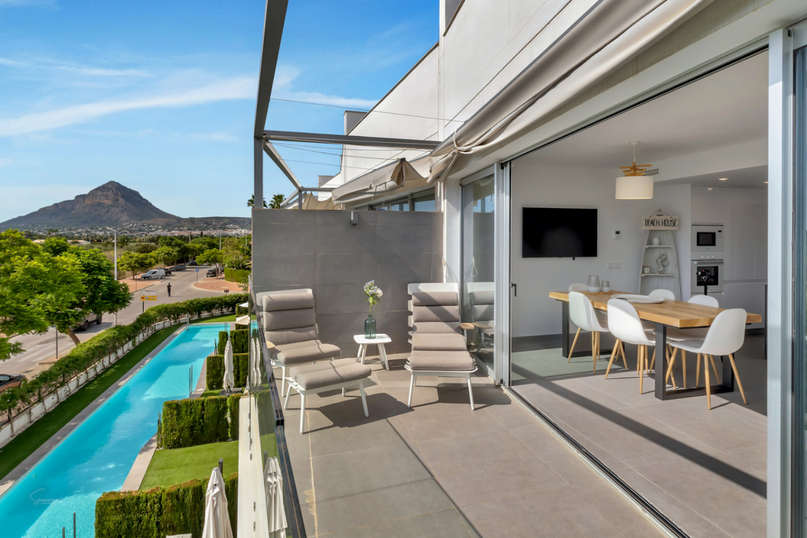 Balcony overlooking the 53-meter community pool and mountain, featuring sun loungers and seamless access to the interior dining area.