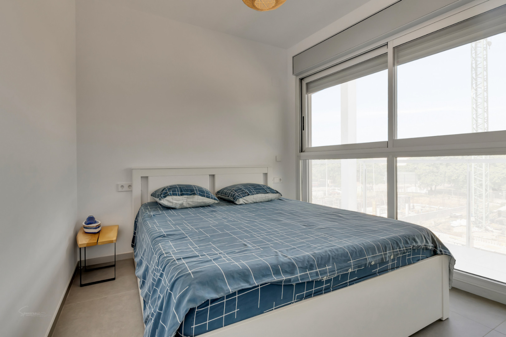 Bright bedroom featuring a double bed and large sliding windows with grey frames and motorized blinds, offering abundant natural light.