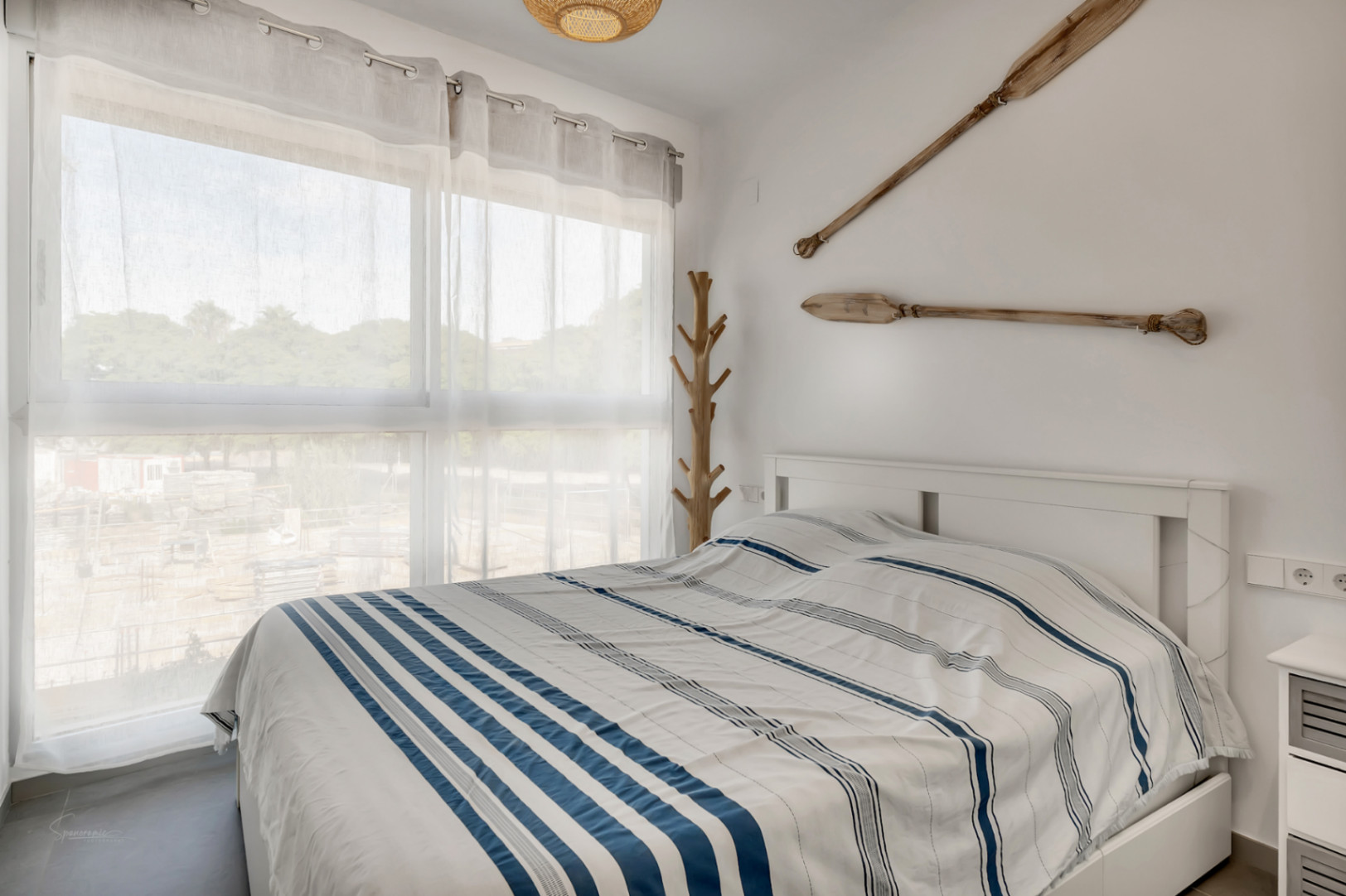 Bright bedroom featuring a nautical theme with decorative wooden oars, a large window providing natural light, and a minimalist white bed frame.
